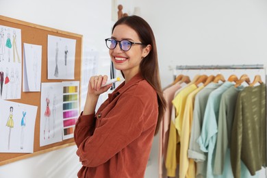 Photo of Fashion designer near corkboard with sketches of clothes in workshop