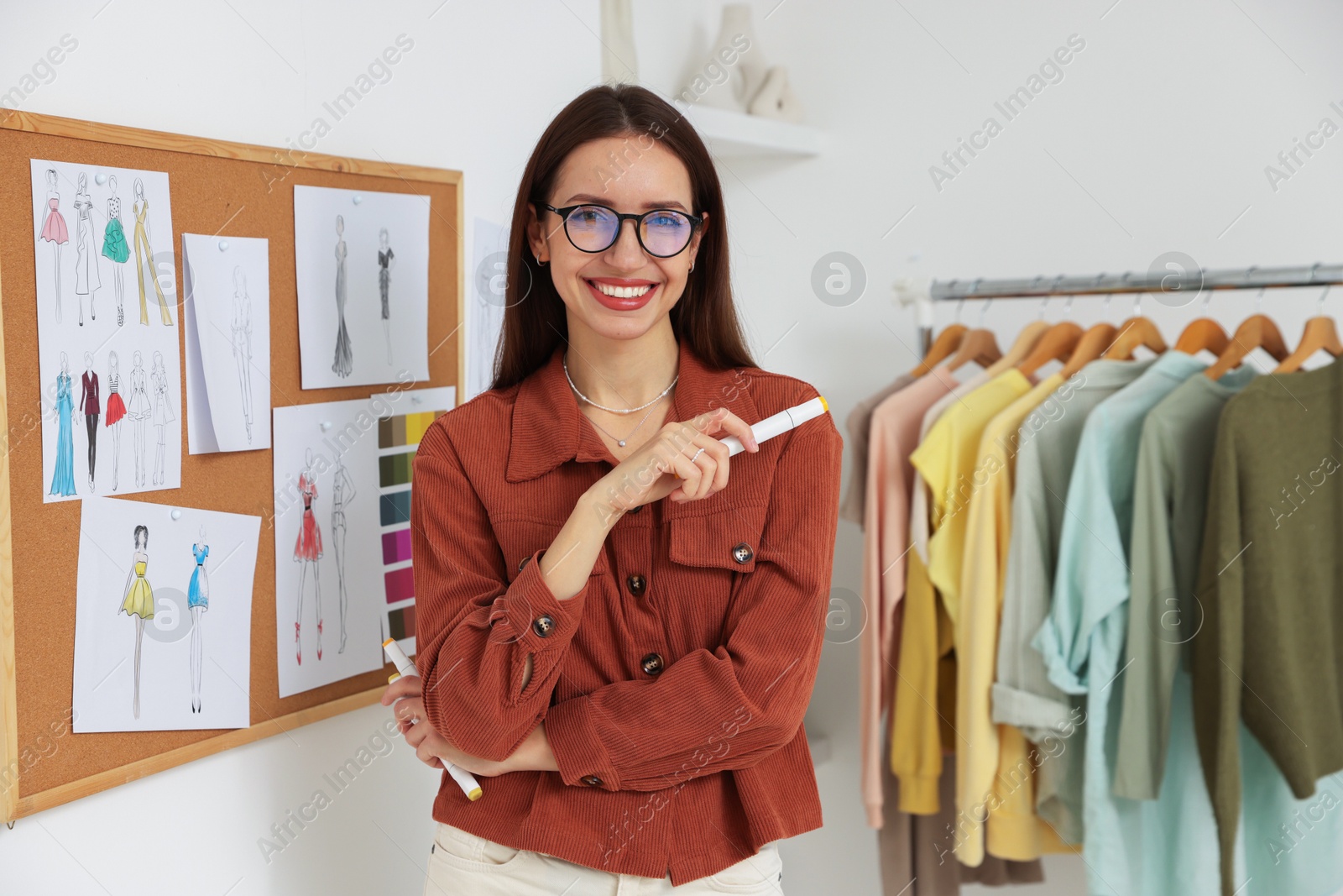 Photo of Fashion designer near corkboard with sketches of clothes in workshop