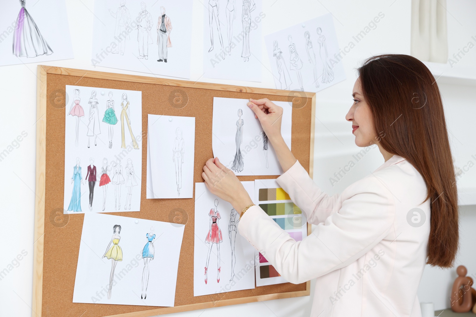 Photo of Fashion designer pinning sketch of clothes to corkboard in workshop