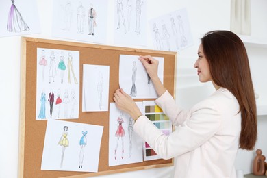 Fashion designer pinning sketch of clothes to corkboard in workshop