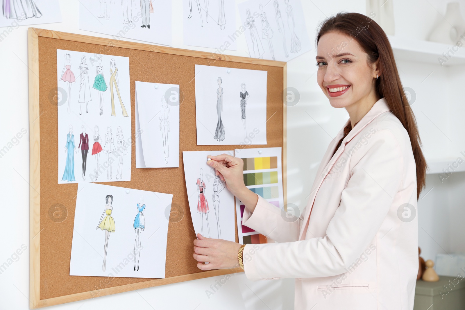 Photo of Fashion designer pinning sketch of clothes to corkboard in workshop