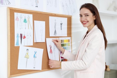 Fashion designer pinning sketch of clothes to corkboard in workshop