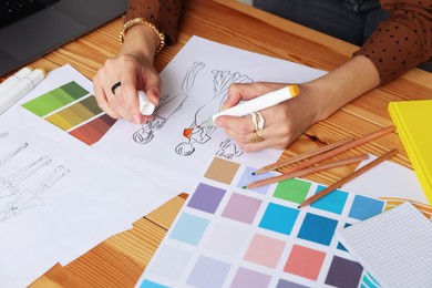 Photo of Fashion designer drawing sketch of clothes at wooden table in workshop, closeup