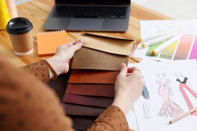 Photo of Fashion designer choosing fabric among colorful samples at wooden table in workshop, closeup