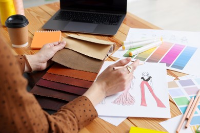 Photo of Fashion designer choosing fabric among colorful samples at wooden table in workshop, closeup