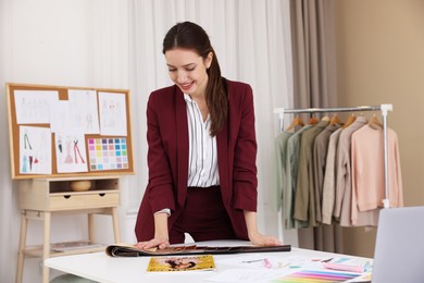 Fashion designer choosing fabric among colorful samples at white table in workshop