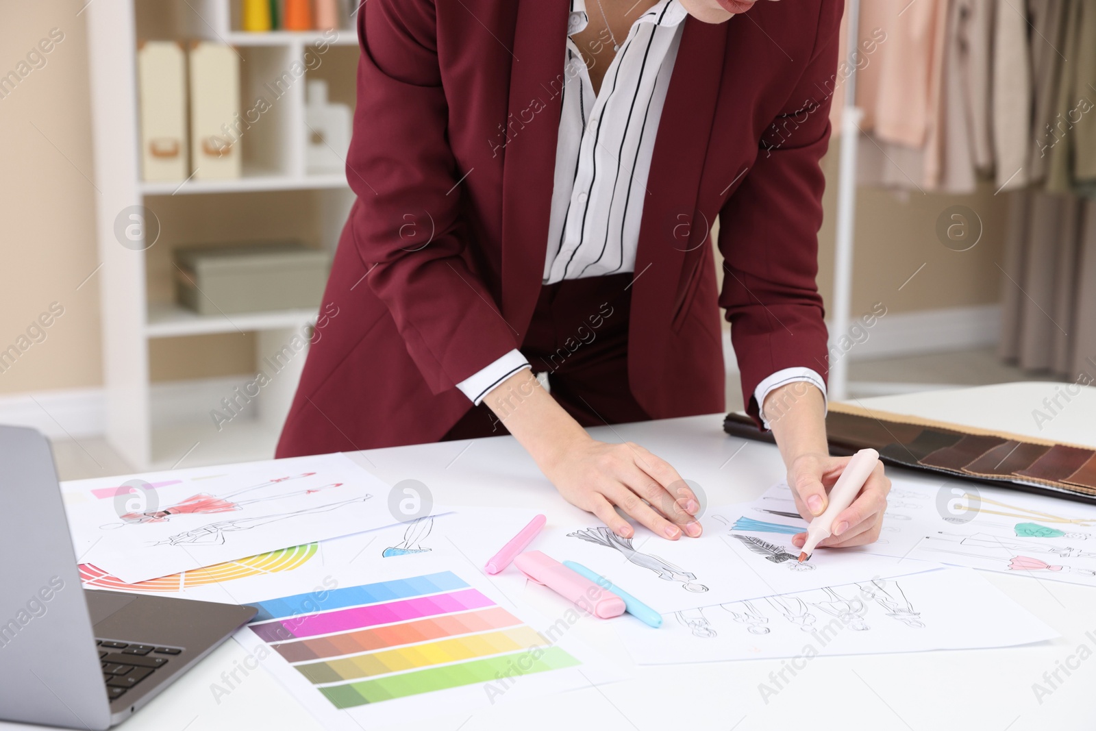 Photo of Fashion designer drawing sketch of clothes at white table in workshop, closeup