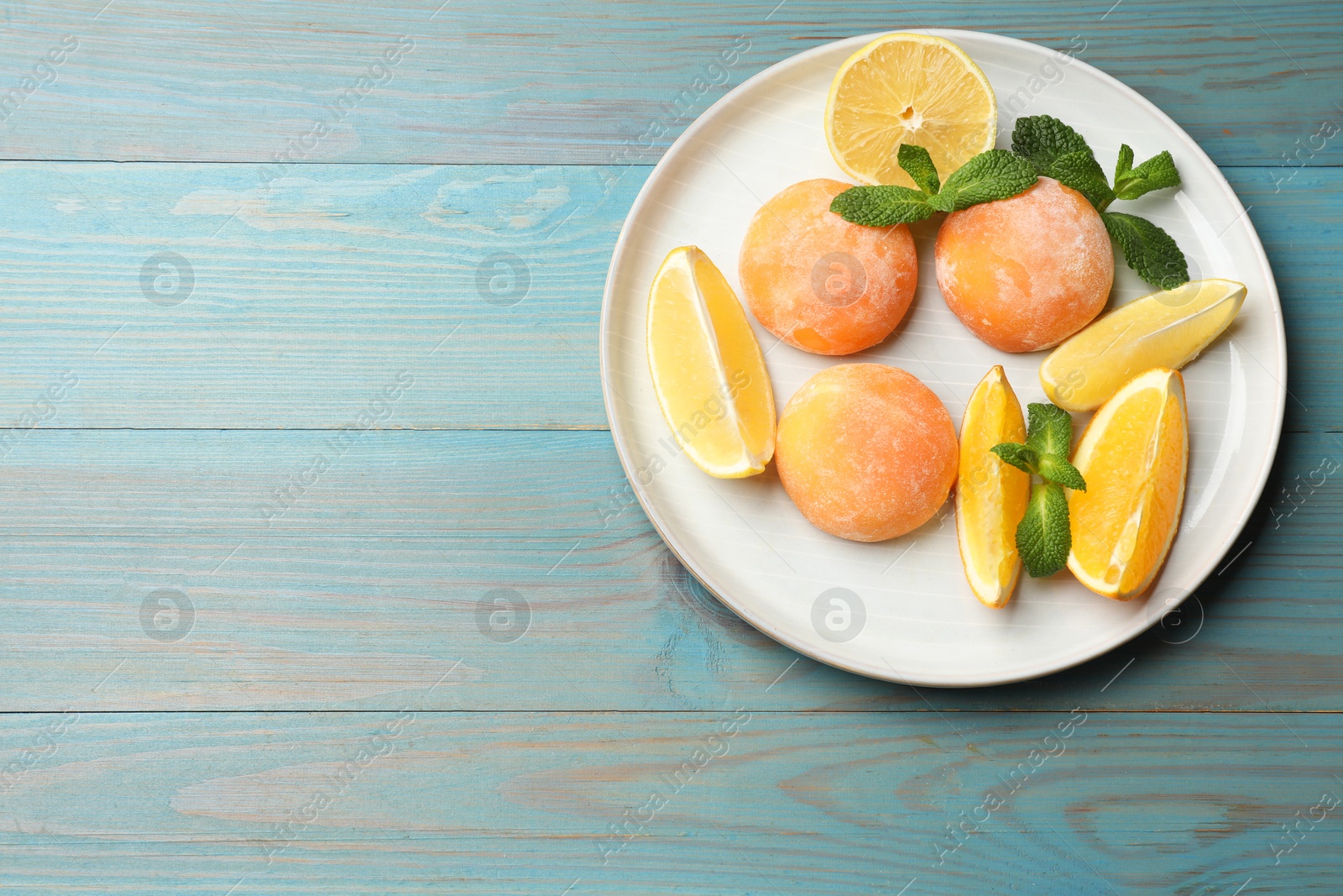 Photo of Tasty mochi, cut orange, lemon and mint on light blue wooden table, top view. Space for text