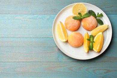 Photo of Tasty mochi, cut orange, lemon and mint on light blue wooden table, top view. Space for text