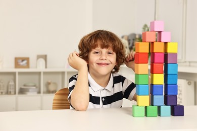 Photo of Little boy playing with stacked colorful cubes at white table indoors