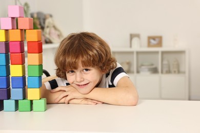 Photo of Little boy playing with stacked colorful cubes at white table indoors, space for text