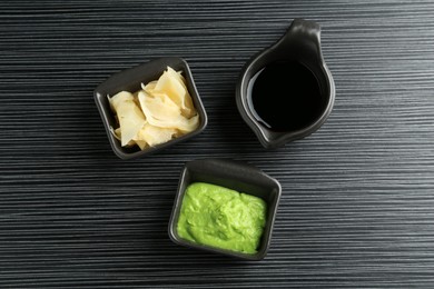 Photo of Hot wasabi paste, soy sauce and ginger on black textured table, flat lay