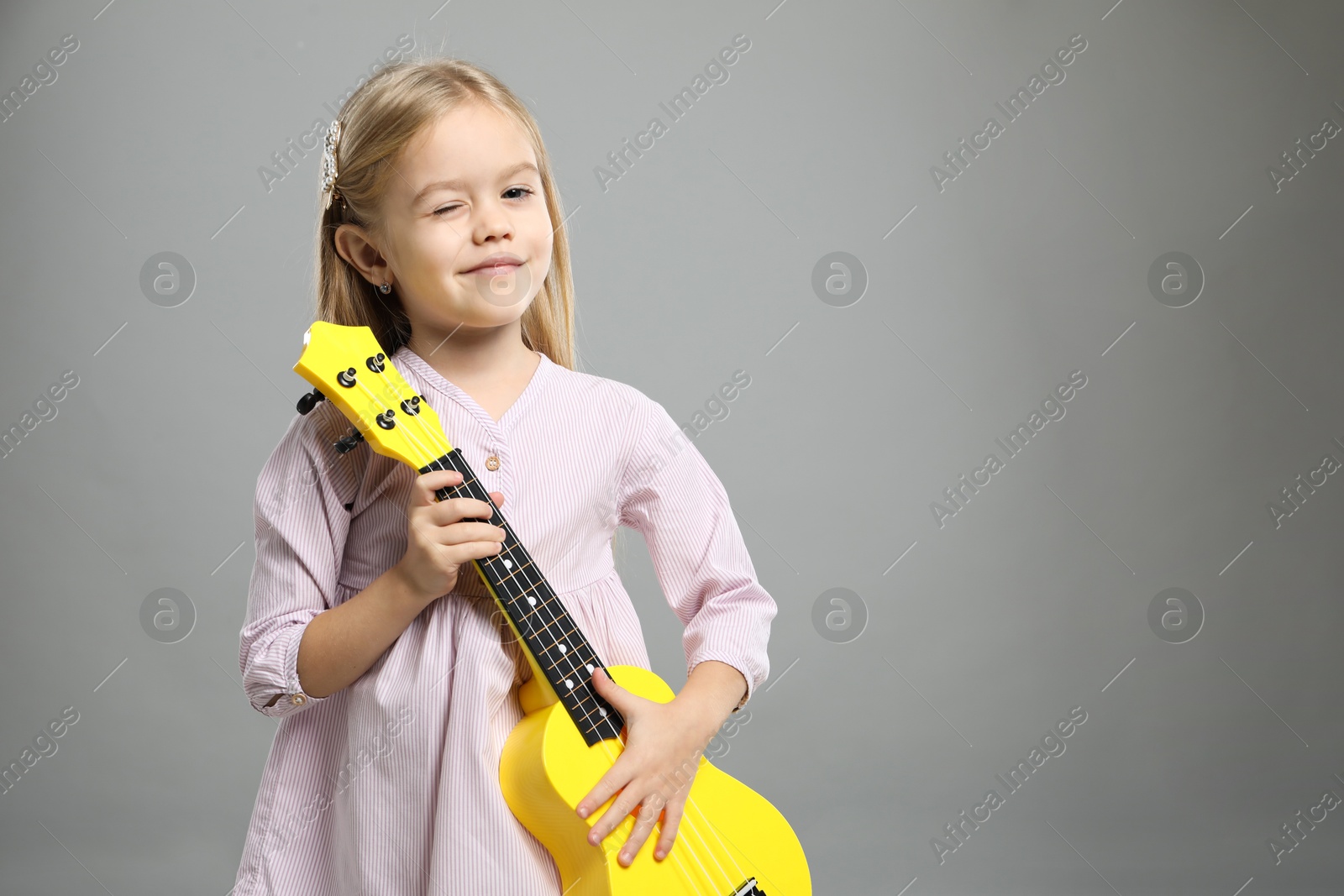 Photo of Little girl with ukulele on gray background, space for text