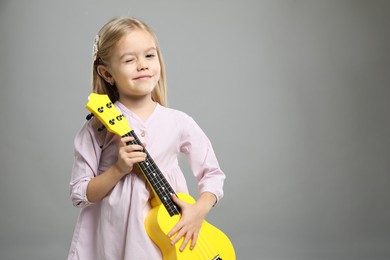 Photo of Little girl with ukulele on gray background, space for text