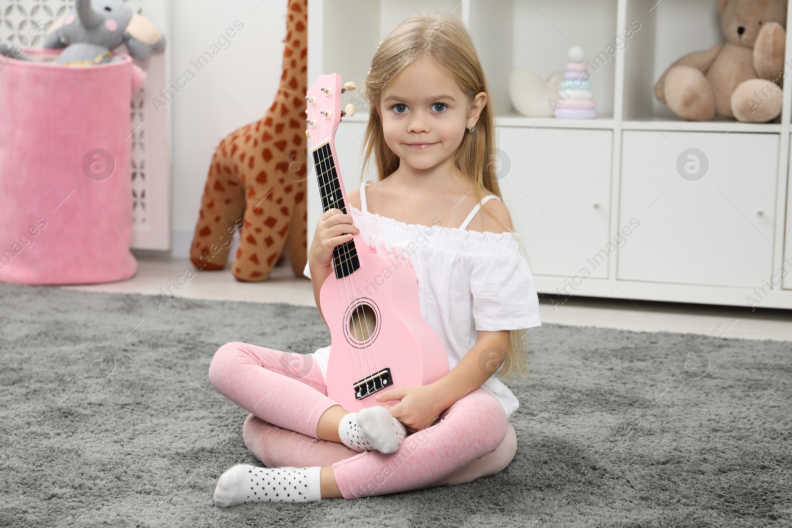 Photo of Little girl with pink ukulele at home