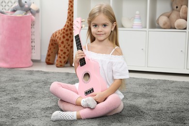 Photo of Little girl with pink ukulele at home