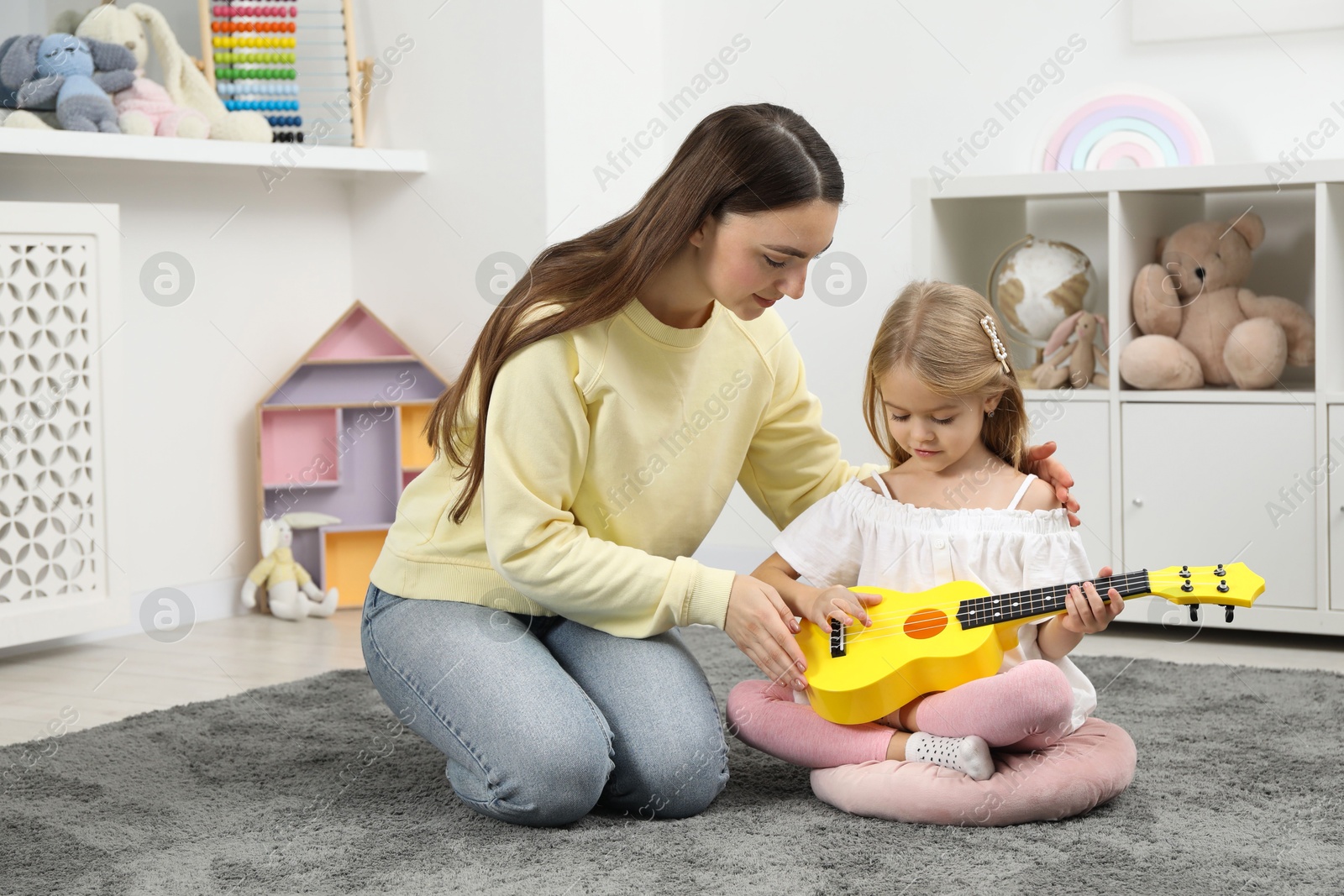 Photo of Young woman teaching little girl to play ukulele at home