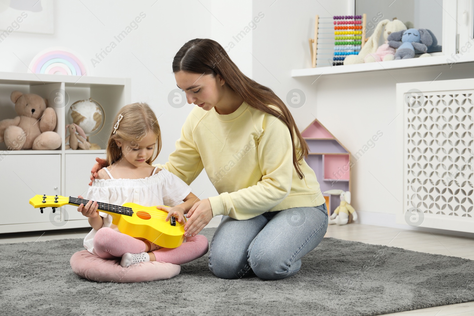 Photo of Young woman teaching little girl to play ukulele at home