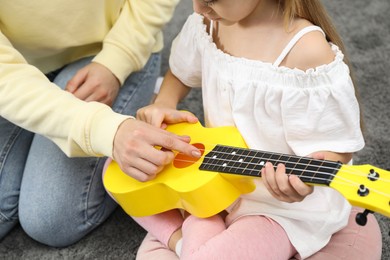 Photo of Woman teaching little girl to play ukulele at home, closeup