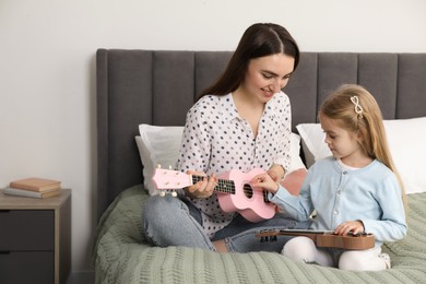 Photo of Young woman teaching little girl to play ukulele at home