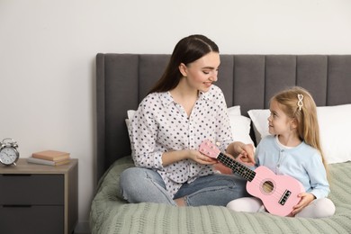 Photo of Young woman teaching little girl to play ukulele at home