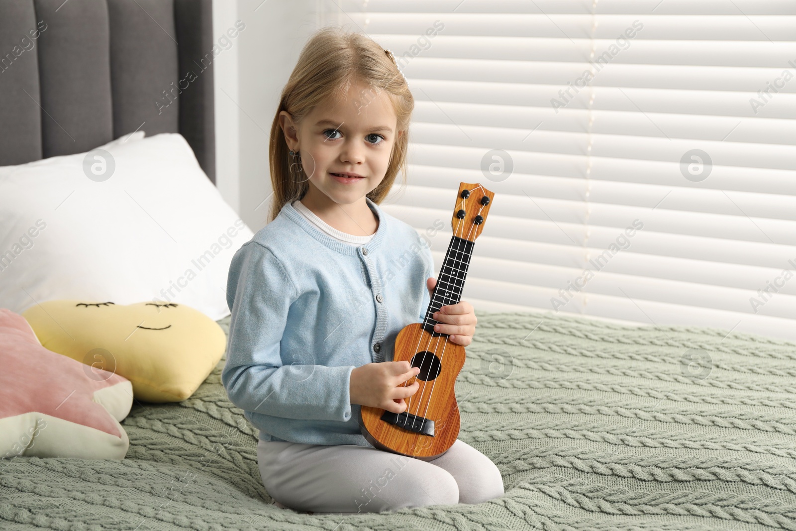 Photo of Little girl with ukulele on bed at home