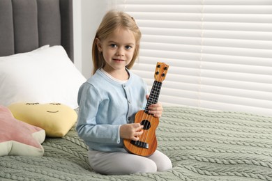 Photo of Little girl with ukulele on bed at home