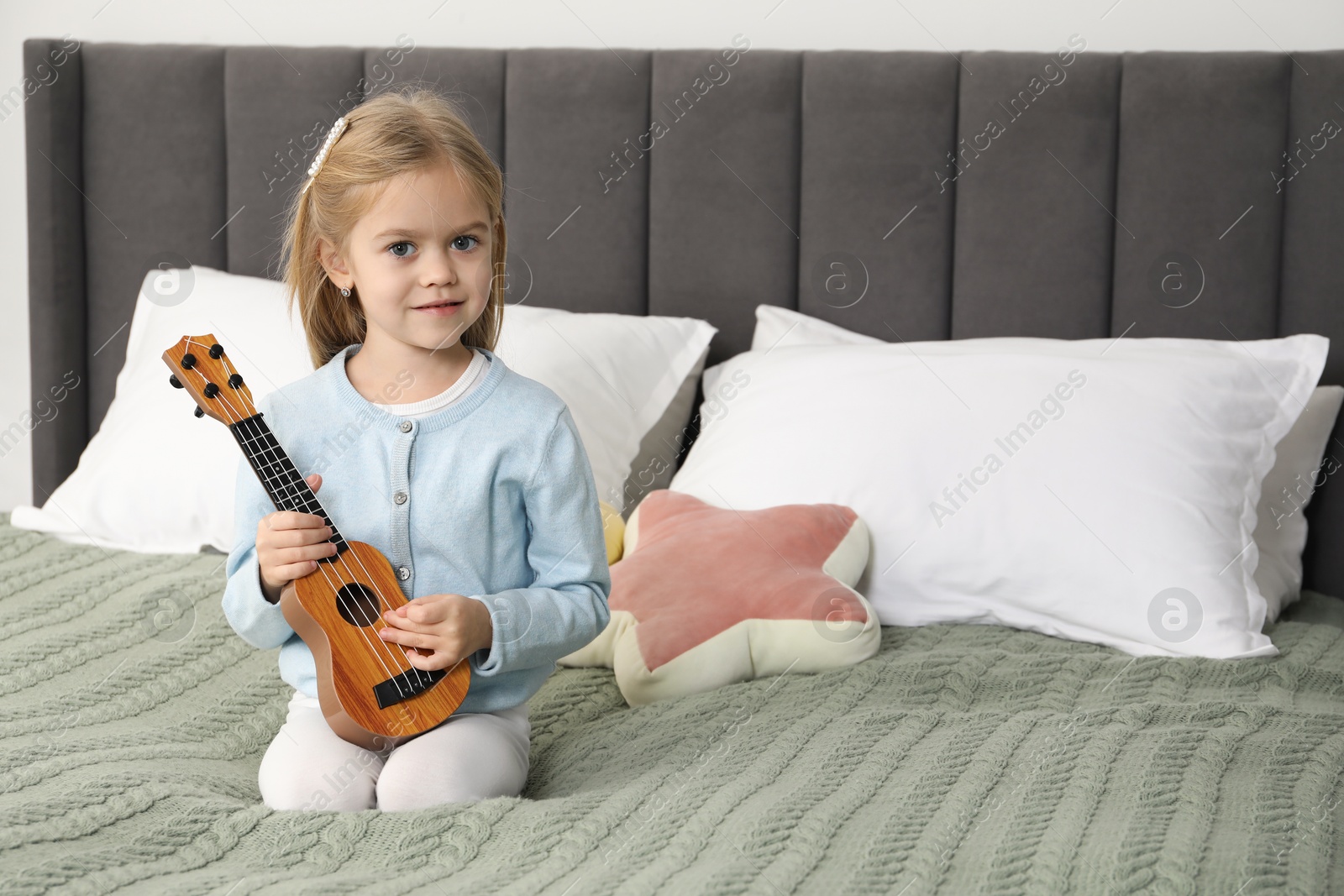 Photo of Little girl with ukulele on bed at home