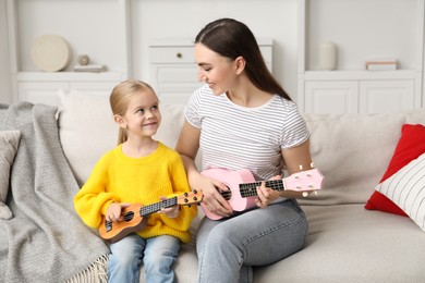 Photo of Young woman teaching little girl to play ukulele at home