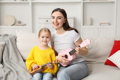 Young woman teaching little girl to play ukulele at home