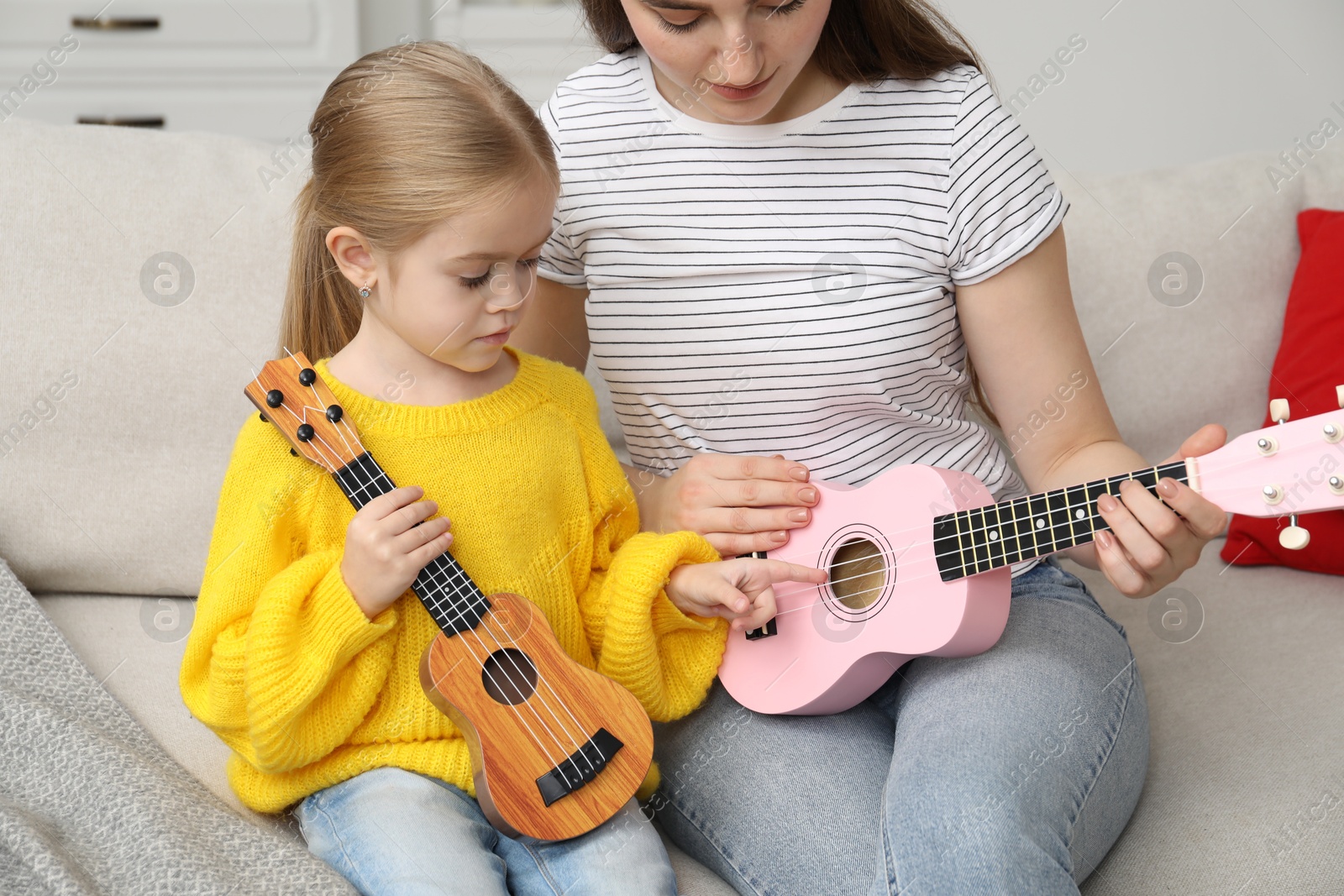 Photo of Young woman teaching little girl to play ukulele at home