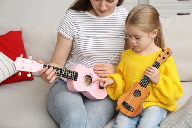 Young woman teaching little girl to play ukulele at home