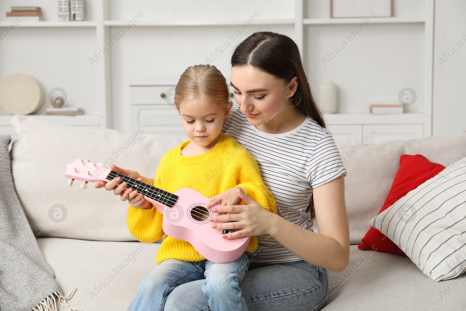 Photo of Young woman teaching little girl to play ukulele at home