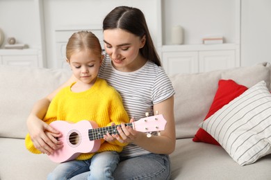 Young woman teaching little girl to play ukulele at home