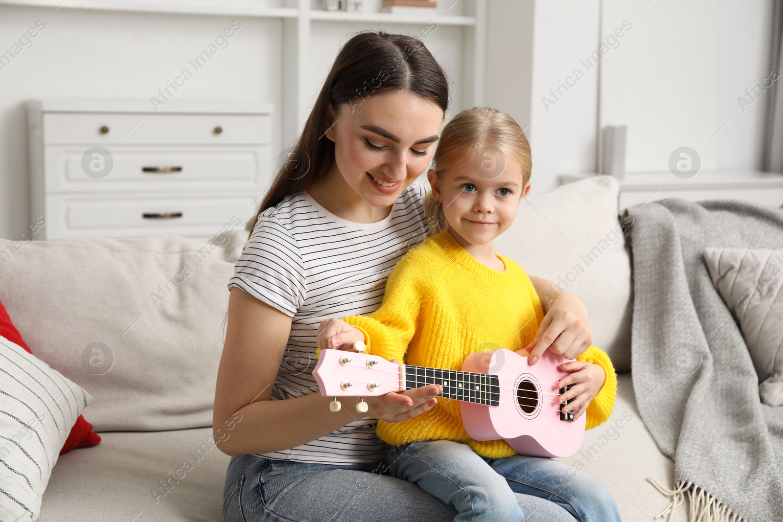 Photo of Young woman teaching little girl to play ukulele at home