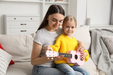 Photo of Young woman teaching little girl to play ukulele at home