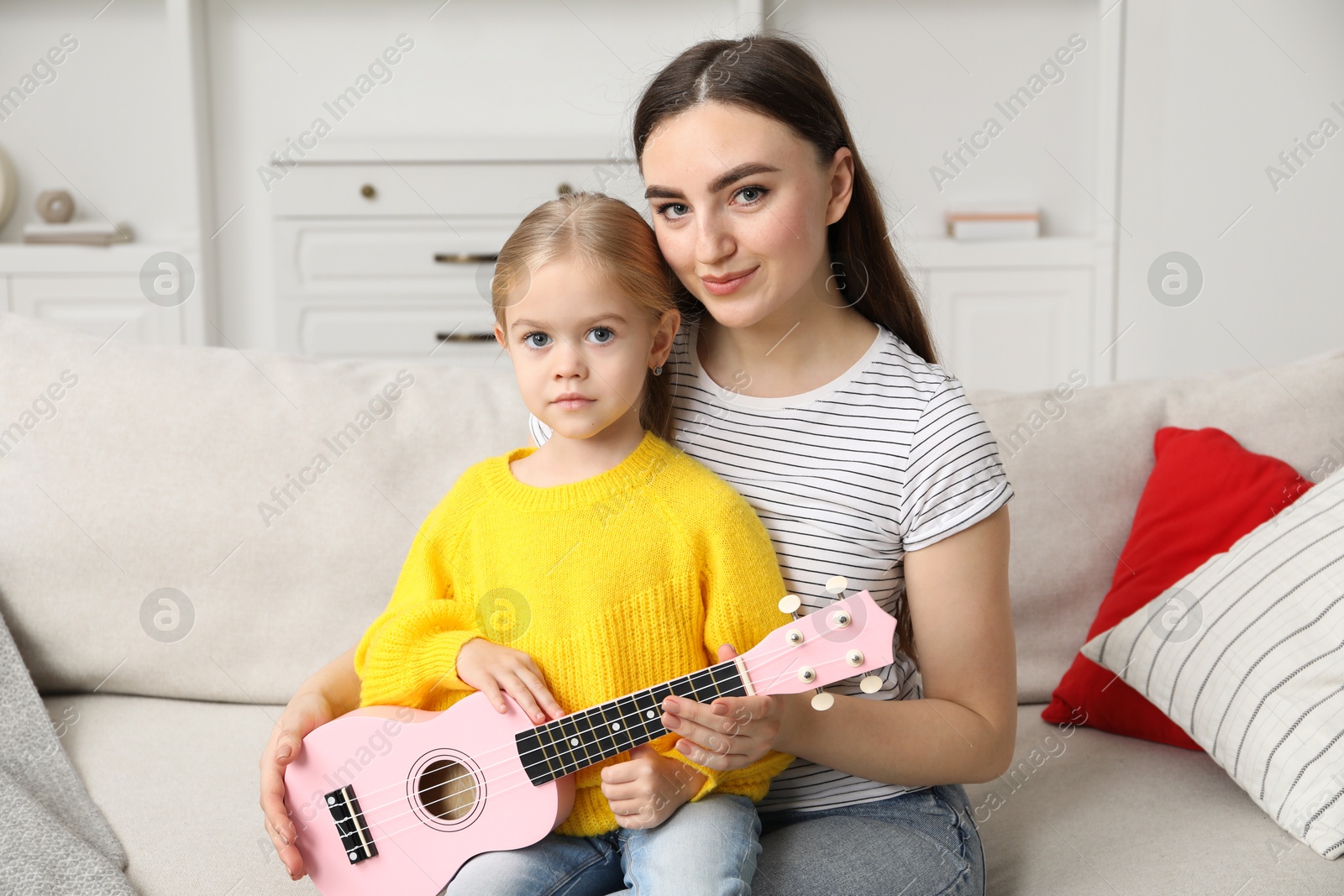 Photo of Young woman and little girl with ukulele on sofa at home