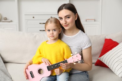 Photo of Young woman and little girl with ukulele on sofa at home