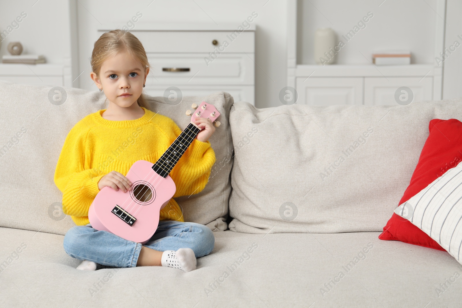 Photo of Little girl with ukulele on sofa at home