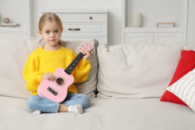 Photo of Little girl with ukulele on sofa at home