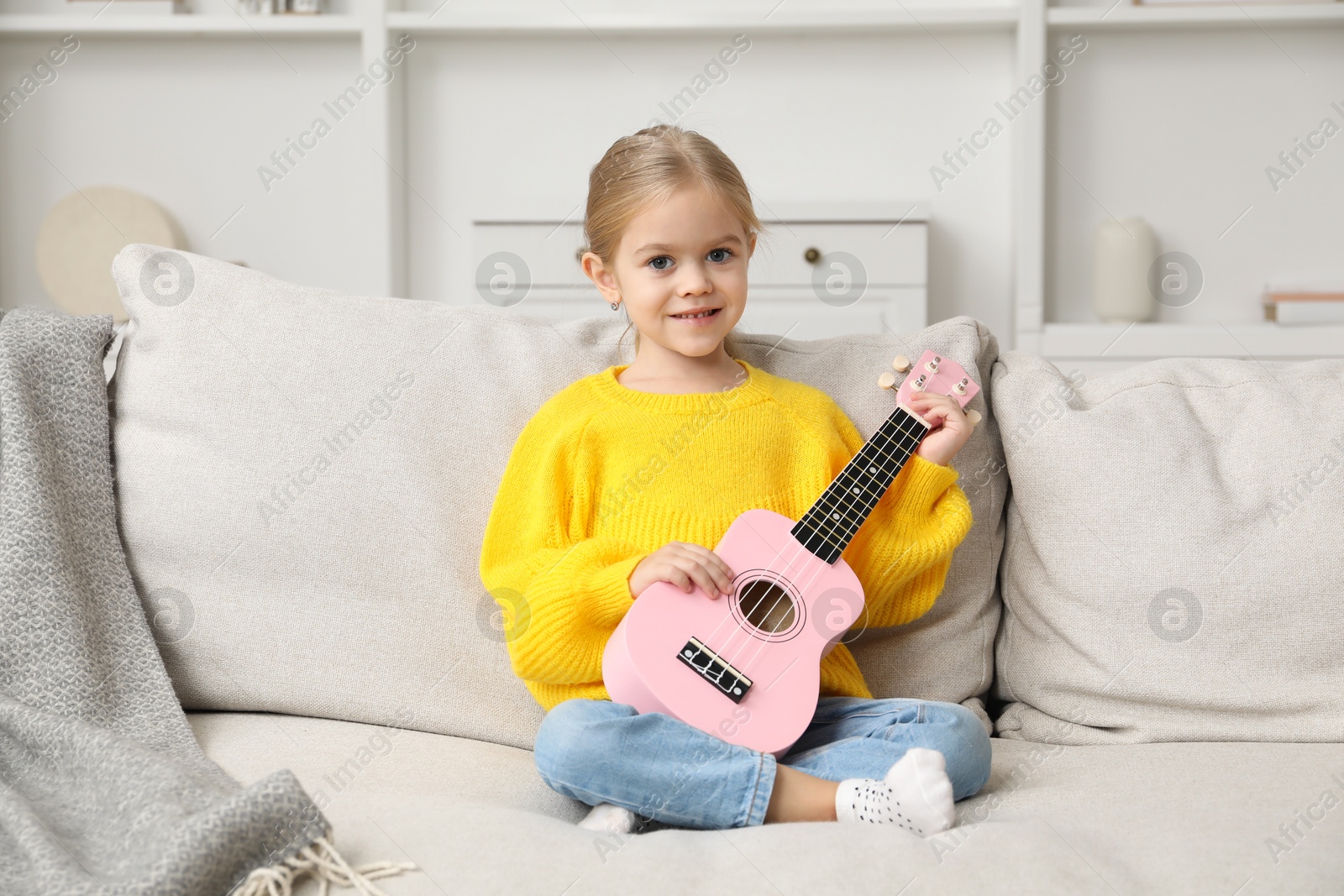 Photo of Little girl with ukulele on sofa at home