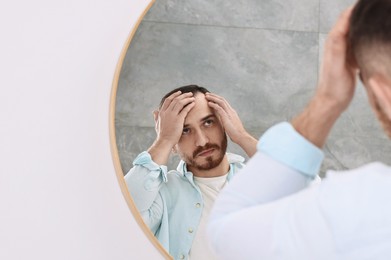 Photo of Baldness problem. Man with receding hairline near mirror in bathroom