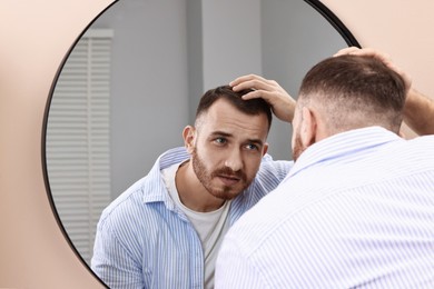 Photo of Baldness problem. Man with receding hairline near mirror in bathroom