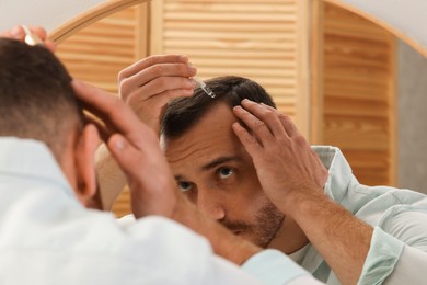 Photo of Baldness treatment. Man applying serum onto hair near mirror at home