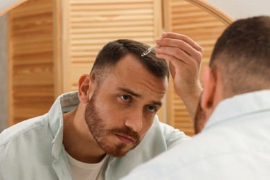 Photo of Baldness treatment. Man applying serum onto hair near mirror at home