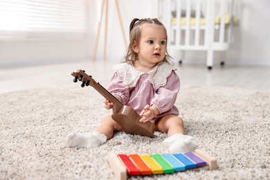 Photo of Cute little girl playing with toy guitar on floor at home