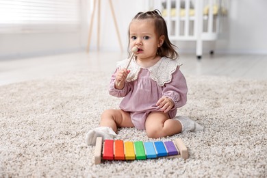 Photo of Cute little girl playing with toy xylophone on floor at home