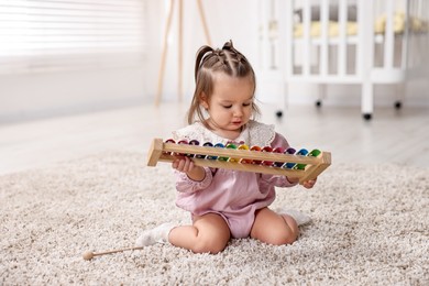 Photo of Cute little girl playing with toy xylophone on floor at home