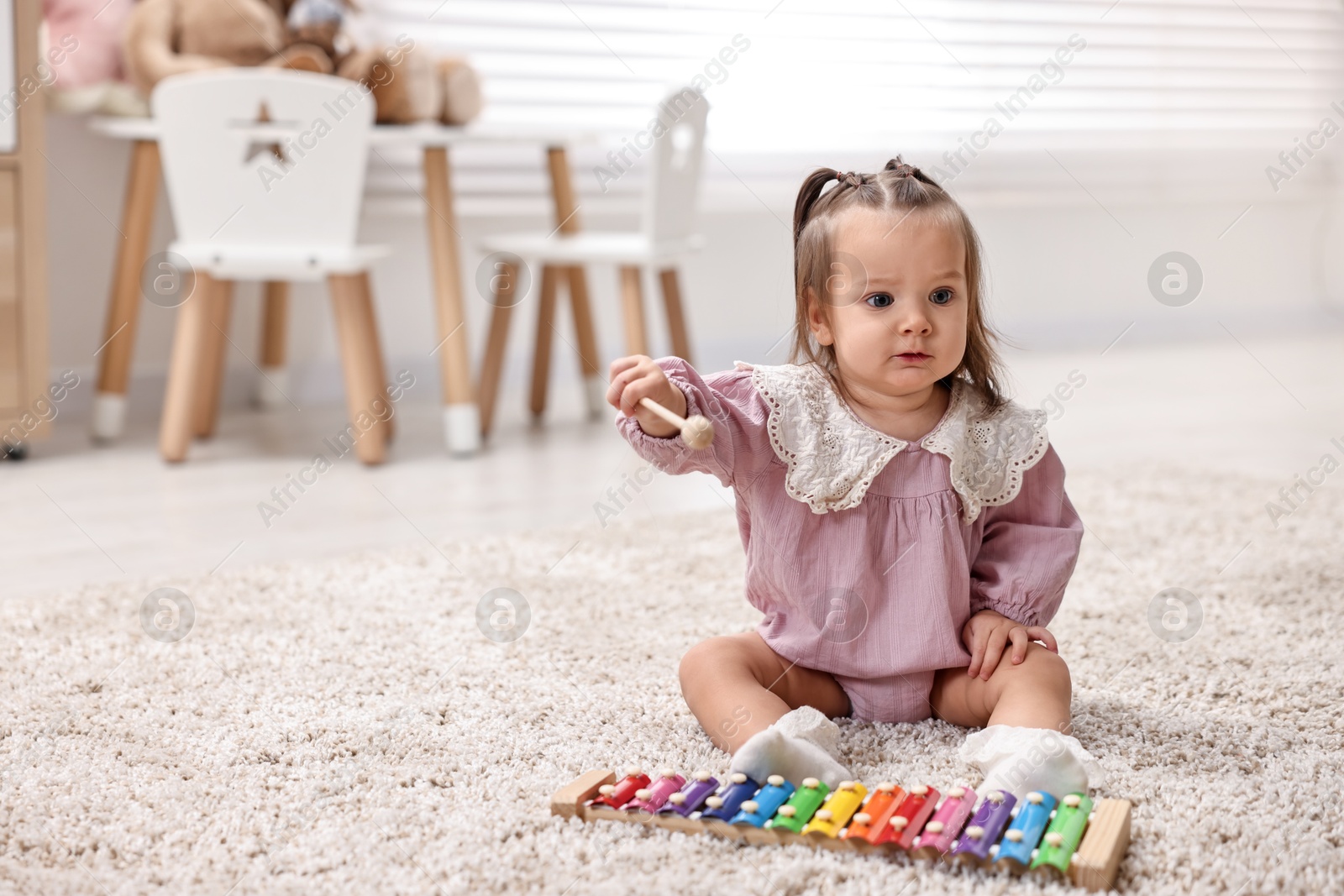 Photo of Cute little girl playing with toy xylophone on floor at home, space for text