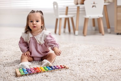 Photo of Cute little girl playing with toy xylophone on floor at home, space for text